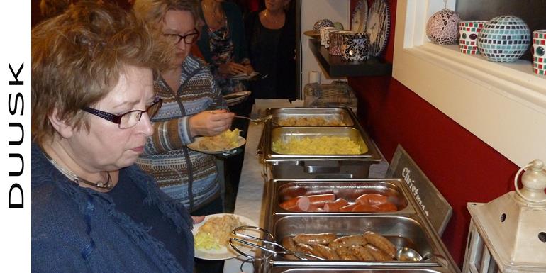 Teambuilding bij DUUSK waarbij ze zelf hun eigen buffet hebben meegebracht. Lekker eten op een lange tafel in grote schalen
															ziet er heerlijk uit. De mensen staan er in een rij voor op te scheppen